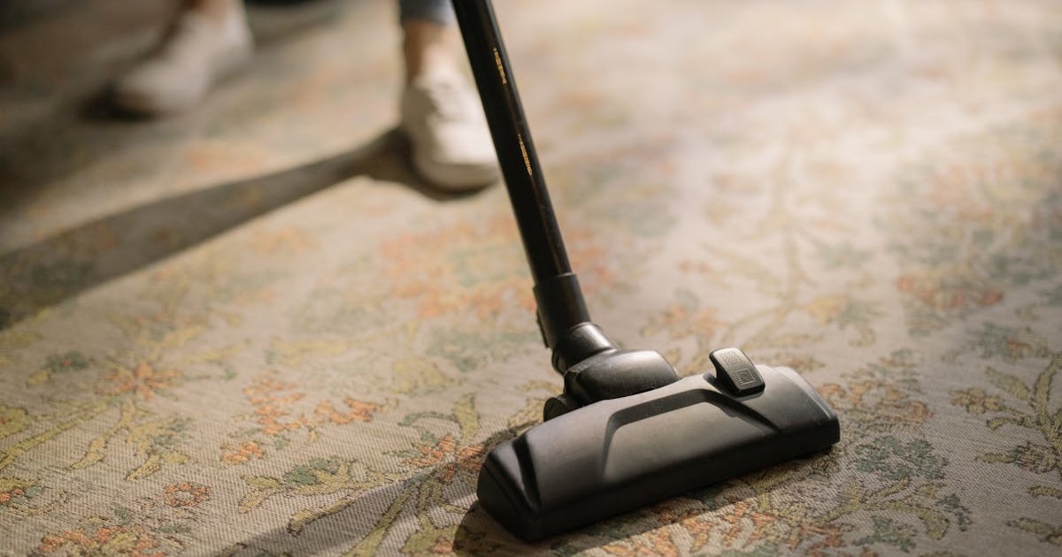Close-up of a vacuum cleaner on a patterned carpet in a sunlit room, capturing a moment of household cleaning.