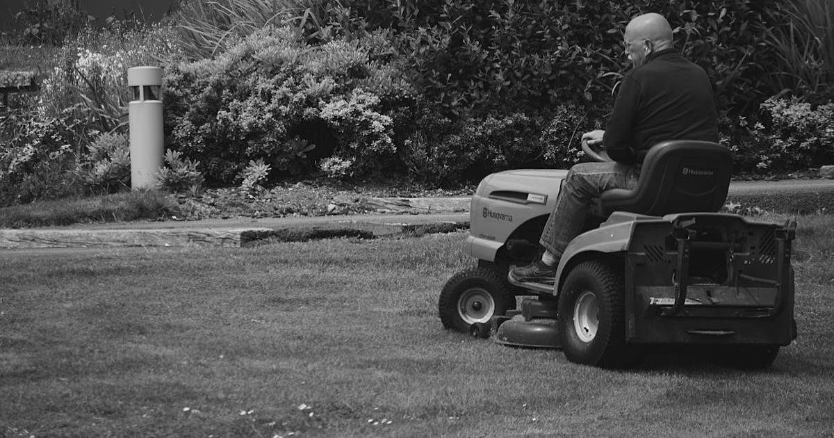 Adult mowing grass on a ride-on lawn mower in a garden setting.