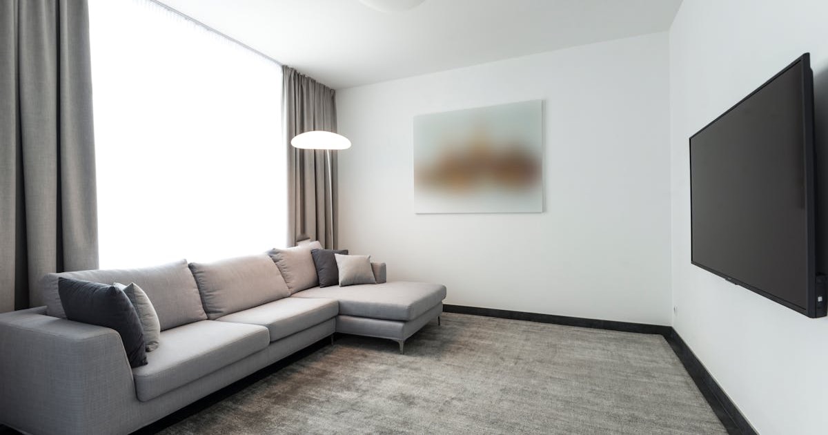 Spacious modern living room with L-shaped grey sofa and flat-screen TV in a minimalist design.