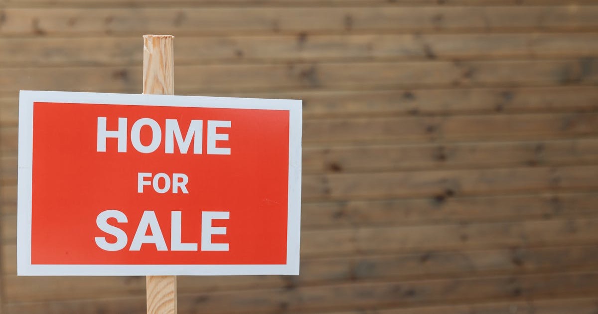 Close-up of a red home for sale sign against a wooden backdrop, ideal for real estate use.