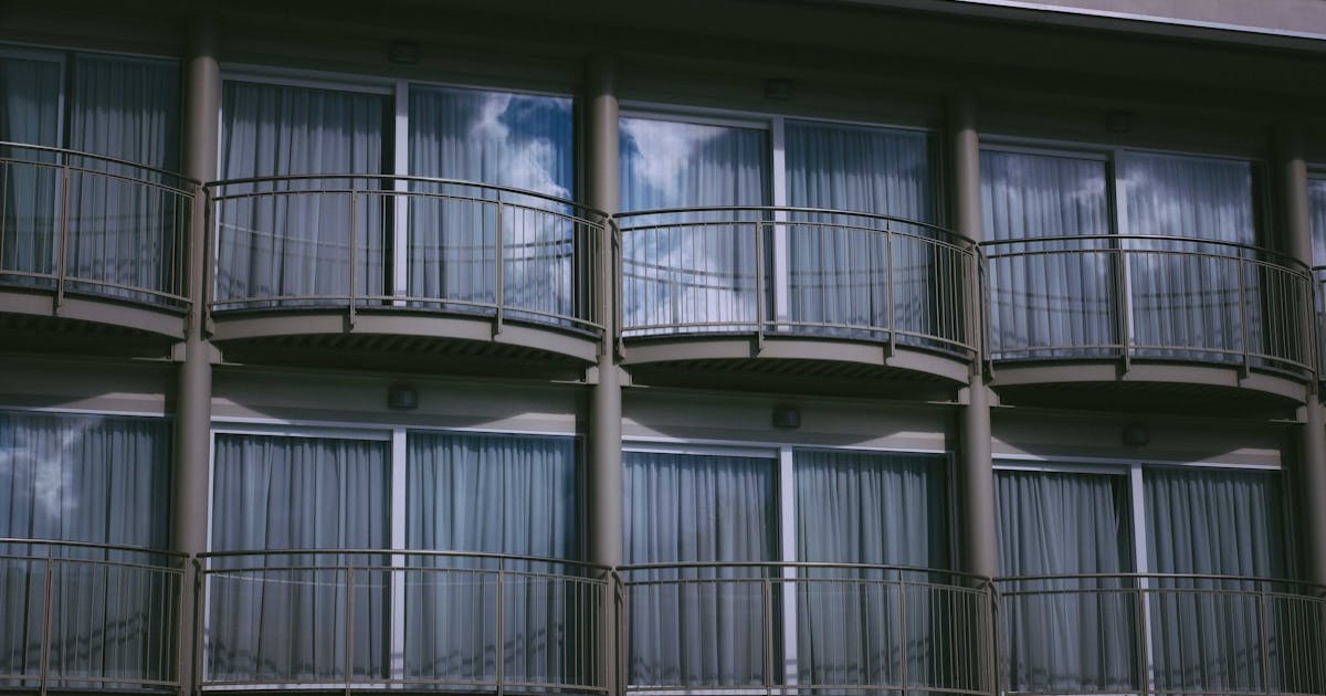 From below balconies with railings and large glass doors and windows with curtains