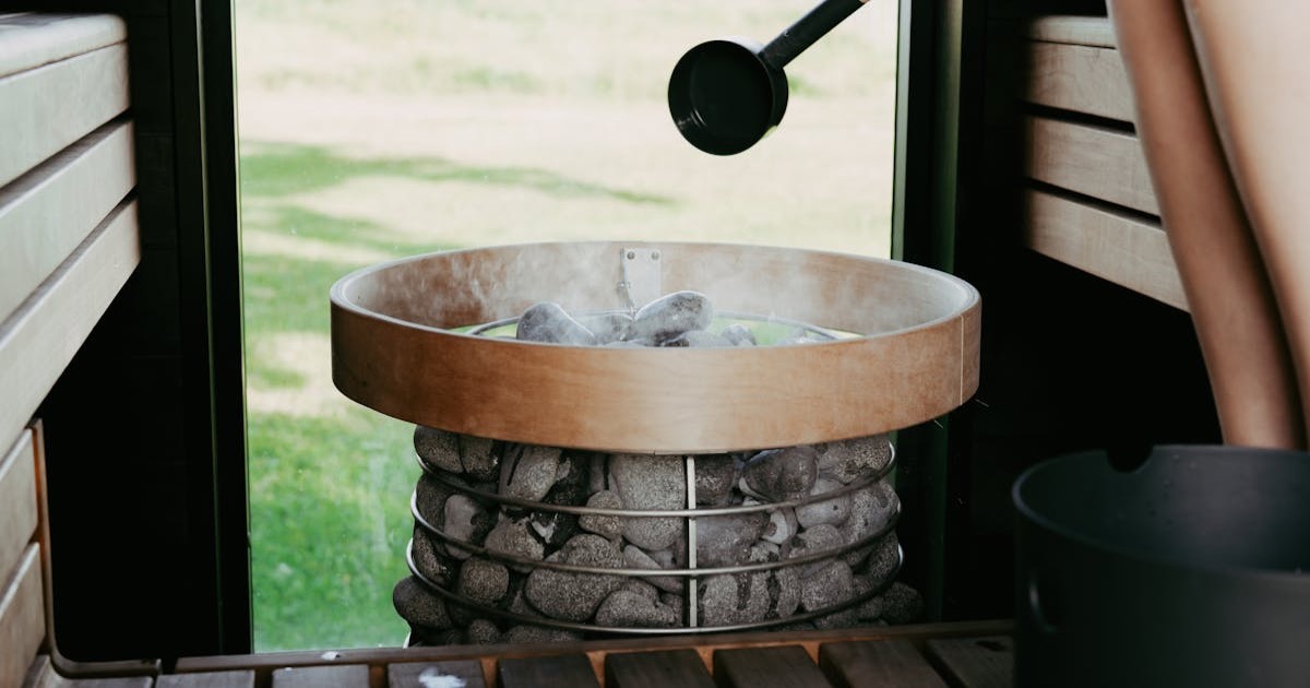 A cozy sauna scene with a person preparing to pour water on hot sauna stones, creating a steamy ambiance.